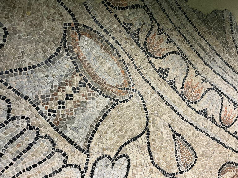 Typische r�mische Ornamentik: Das Motiv besteht aus: schwarzen Konturlinien (Tesserae aus Basalt oder dunklem Kalkstein), hellen F�llfl�chen (Kalkstein, Marmor) und r�tlichen Akzenten (Ziegel, Terrakotta oder roter Stein). Die geschwungenen Formen geh�ren