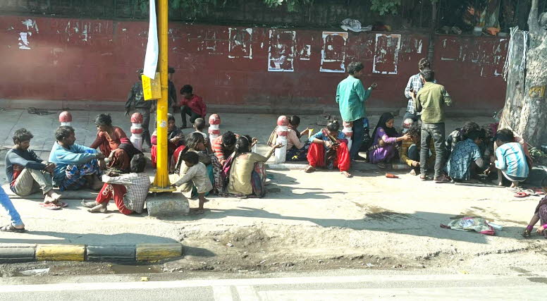 Fl�chtlinge aus Bangla Desch: Auf dem Foto ist eine gr��ere Gruppe von Menschen � darunter viele Kinder � zu sehen, die am Stra�enrand in Delhi sitzen. Sie wirken, als w�rden sie warten, essen oder sich gegenseitig versorgen. Das Ganze spielt sich im �ffe