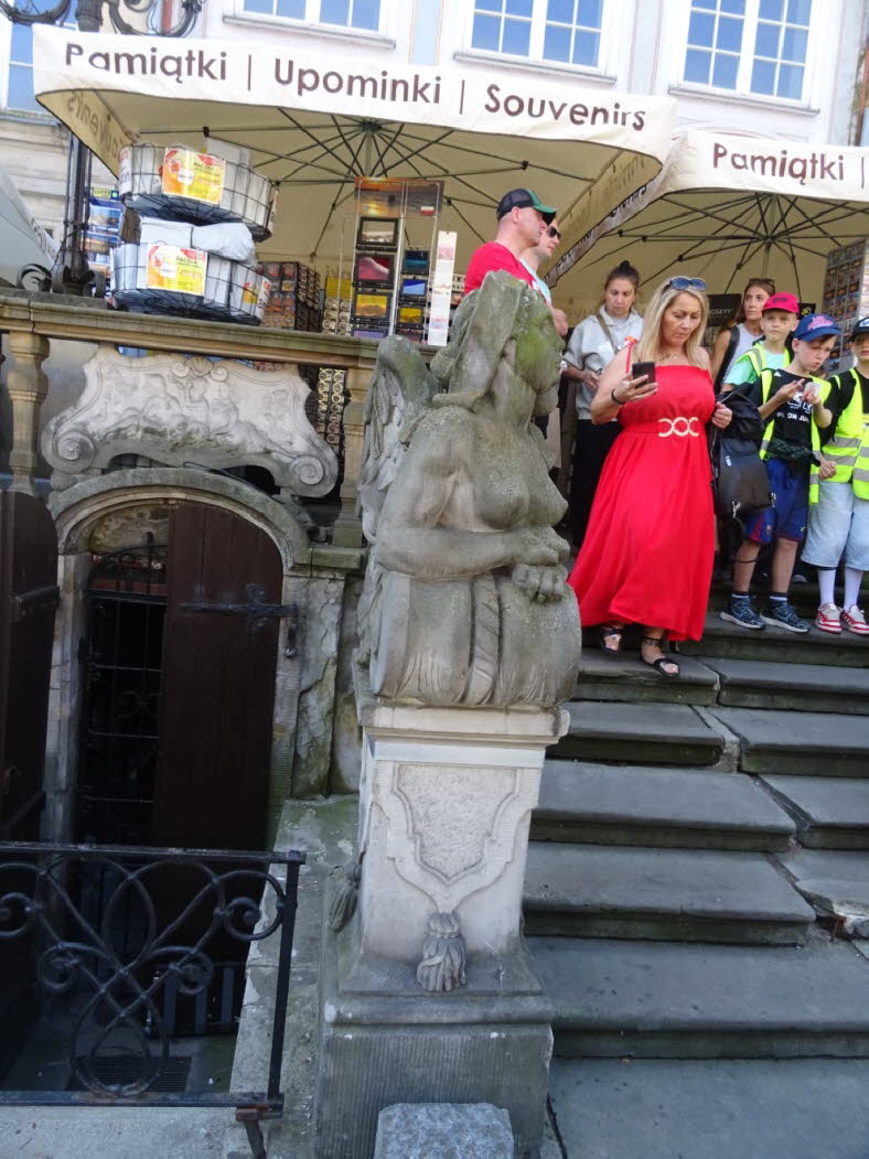 Diese Steinskulptur im Bild stellt ein Fabelwesen mit einem menschlichen Oberk�rper und einem gefl�gelten L�wenk�rper dar. Sie �hnelt einer klassischen Sphinx und bewacht als historisches Denkmal den Treppenaufgang zu einem alten Geb�ude. Hier sind weiter
