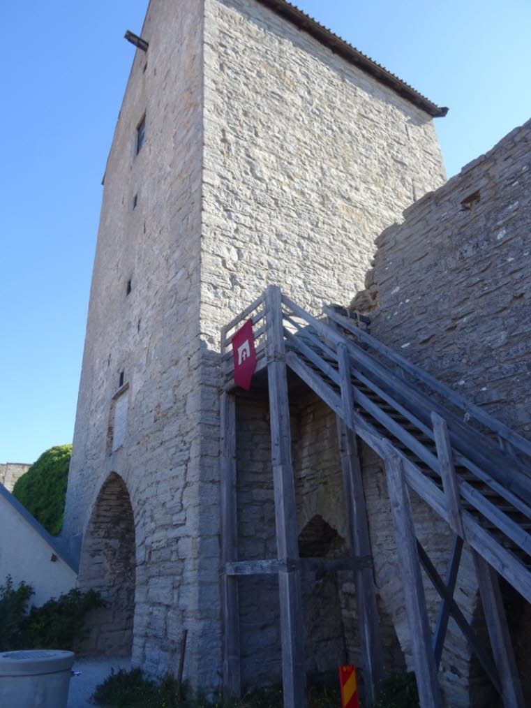 Das Wappen von Visby zeigt ein Agnus Dei (das Lamm Gottes) mit einer Fahne. Der markante rot-wei�e Wimpel, den Sie auf dem Bild sehen, nimmt genau auf diese Farben Bezug. Die Holzkonstruktion im Bild dient als Treppenaufgang, um Teile der historischen Mau
