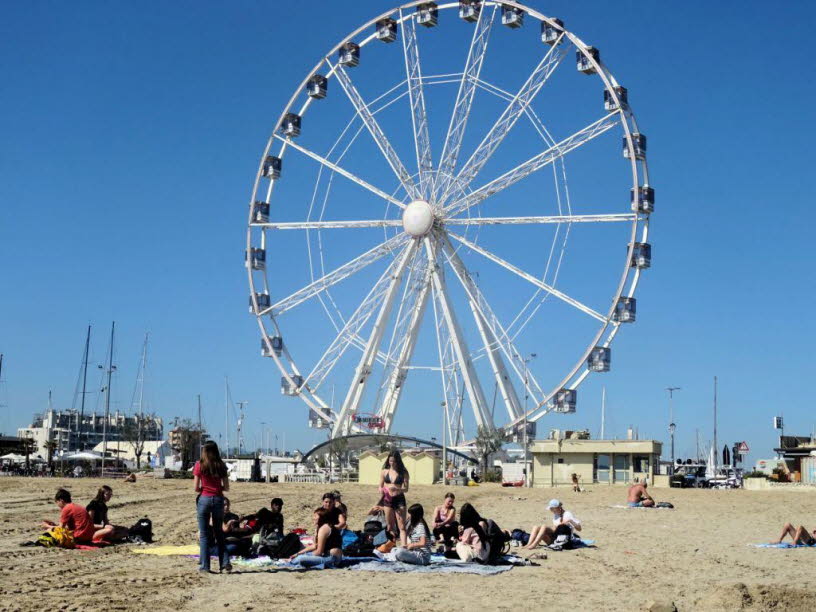 Dieses Foto � Strand, Riesenrad, Marina � ist der perfekte Kontrapunkt zu den bisherigen Fotos Serie. Es zeigt den anderen Pol der Adria: nicht Arbeit, sondern Freizeit. Nicht Fischerei, sondern Tourismus. Und genau dieser Gegensatz ist entscheidend, wenn