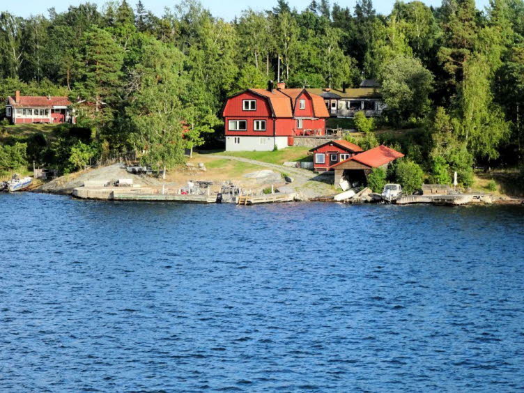 Das Bild zeigt eine idyllische K�stenlandschaft im Stockholmer Sch�rengarten (Stockholms sk�rg�rd) in Schweden. Die felsigen Inseln mit ihrem dichten Baumbestand und traditionellen, roten Holzh�usern bestimmen die Landschaft.