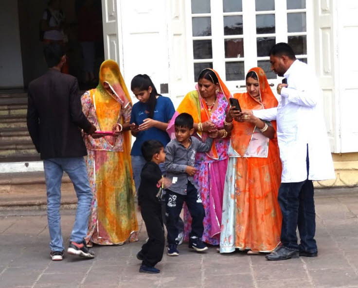 32 Unsere Inder (2)Auf dem Bild ist eine Gruppe von sieben Personen zu sehen, die vor dem Eingang eines hellen Geb�udes stehen. Bei den Personen handelt es sich um eine Familie oder Gruppe von Freunden in traditioneller indischer Kleidung, die wahrscheinl