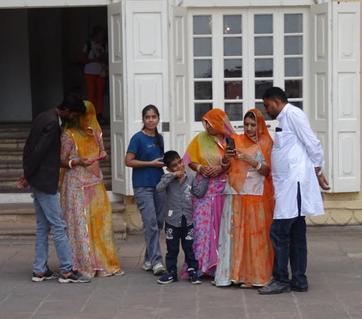 Auf dem Bild ist eine Gruppe von sieben Personen zu sehen, die vor dem Eingang eines hellen Geb�udes stehen. Bei den Personen handelt es sich um eine Familie oder Gruppe von Freunden in traditioneller indischer Kleidung, die wahrscheinlich aus der Region 