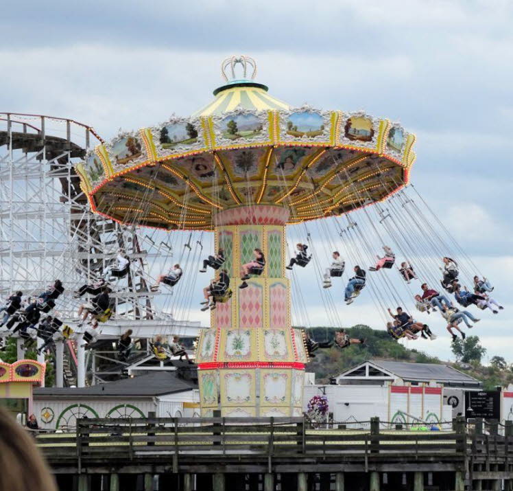 Auf dem Bild ist ein klassisches Kettenkarussell, oft auch als Wellenflug bezeichnet, in einem Vergn�gungspark zu sehen. Im Hintergrund befindet sich eine h�lzerne Achterbahn.
