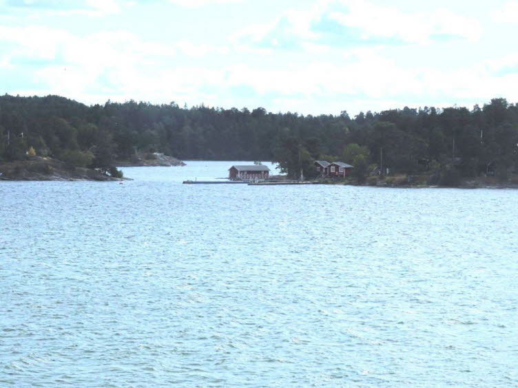Das Bild zeigt eine Szene auf der idyllischen Insel Lilla B�tsholmen im Stockholmer Sch�rengarten. Die Insel ist typisch f�r die Region und bekannt f�r ihre felsige K�ste und die traditionellen roten Holzh�user.