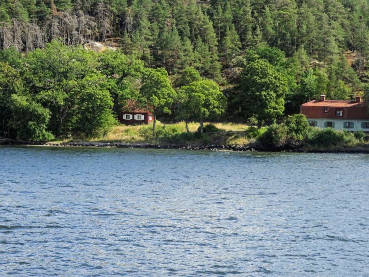 Dieses Bild zeigt zwei traditionelle, rot gestrichene Holzh�user (Schwedenh�user) mit wei�en Fensterrahmen und roten Ziegeld�chern, die idyllisch am Ufer eines Sees oder der K�ste liegen.