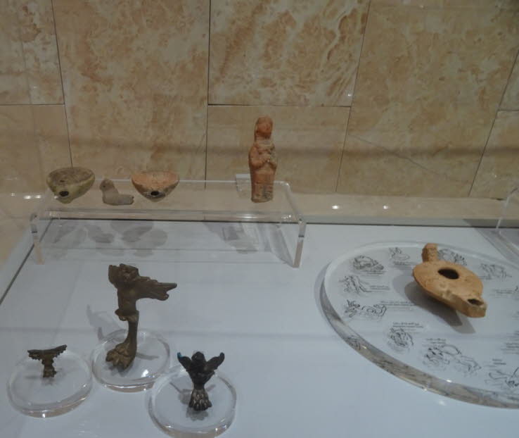 Terrakotta-�llampen: Mehrere antike Ton-�llampen sind in der oberen Reihe und eine markante, flache Lampe mit Verzierungen liegt auf einer runden Platte in der unteren rechten Ecke. �llampen waren zentrale Lichtquellen im Alltag und bei Ritualen im Altert