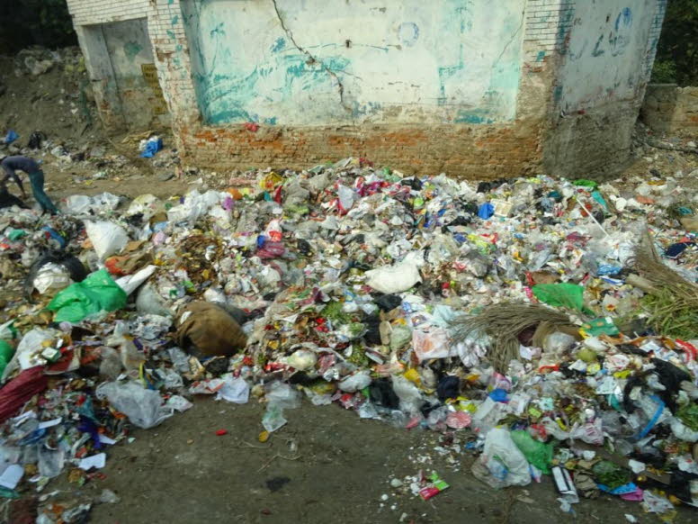 Auf dem Bild ist ein gro�er, unkontrollierter M�llhaufen zu sehen, der sich am Rand einer informellen Siedlung oder Baustelle befindet. Der Haufen besteht aus einer Vielzahl von Haushaltsabf�llen, darunter viele bunte Plastikt�ten, Flaschen und organische
