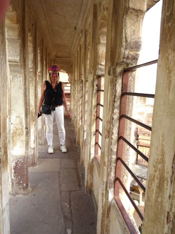 Das Bild zeigt eine Frau, die durch einen historischen Korridor oder Wandelgang im Mehrangarh Fort in Jodhpur, Rajasthan, Indien, geht.