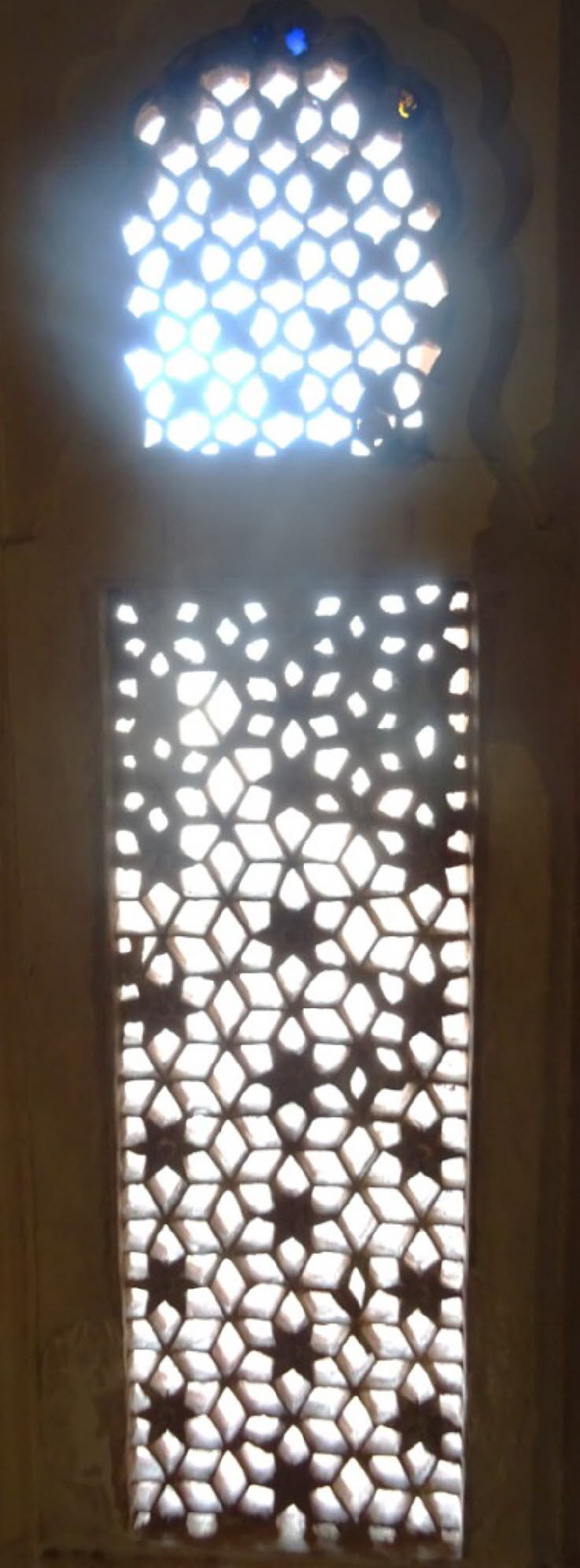 Das Bild zeigt ein kunstvoll geschnitztes Jali-Gitterfenster in Indien. Jali ist ein traditionelles Architekturelement, das in der indischen und indo-islamischen Baukunst weit verbreitet ist. Details zu Jali-Fenstern Zweck: Die perforierten Gitter dienen 