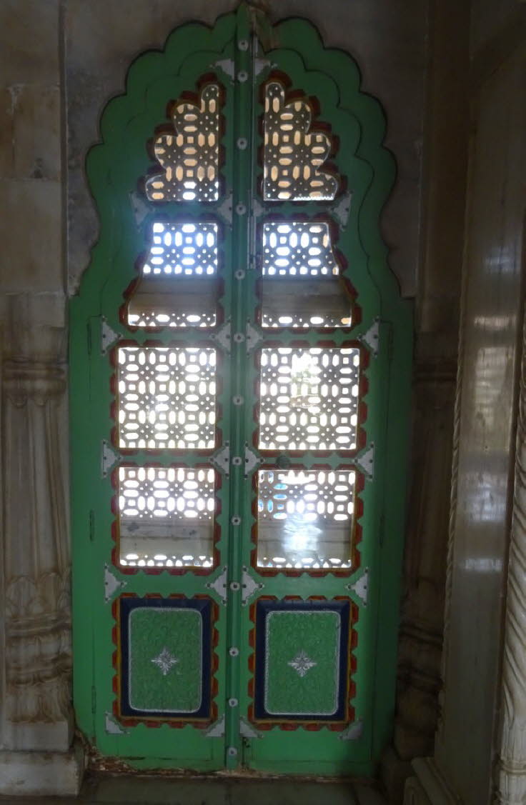 Das Bild zeigt eine kunstvoll bemalte, gr�ne Jali-T�r oder ein Fenster mit durchbrochenen Gitterschnitzereien.  Architektur: Die T�r kombiniert traditionelle Rajputen- und Mogul-Stile. Der Bogen oben und die rechteckigen Paneele sind mit komplexen, geschn