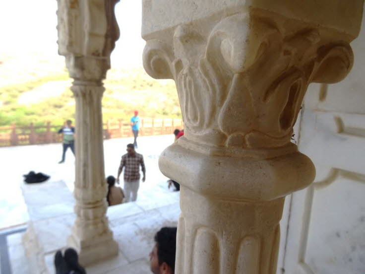 Das Bild zeigt einen Innenraum mit kunstvoll geschnitzten, hellen Steins�ulen und einem Marmorboden, die typisch f�r die traditionelle indische Architektur sind.  