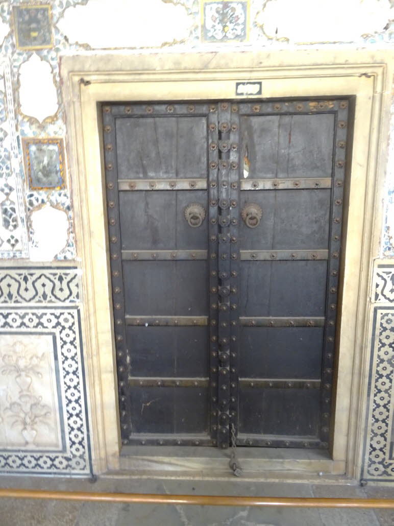 Die Aufnahme zeigt eine reich verzierte T�r, die typisch f�r die Architektur in S�dasien ist, wie sie im Sheesh Mahal (Spiegelpalast) in Indien zu finden ist. Die Doppelt�r besteht aus dunklem Holz oder Metall und ist mit zahlreichen Nieten und horizontal