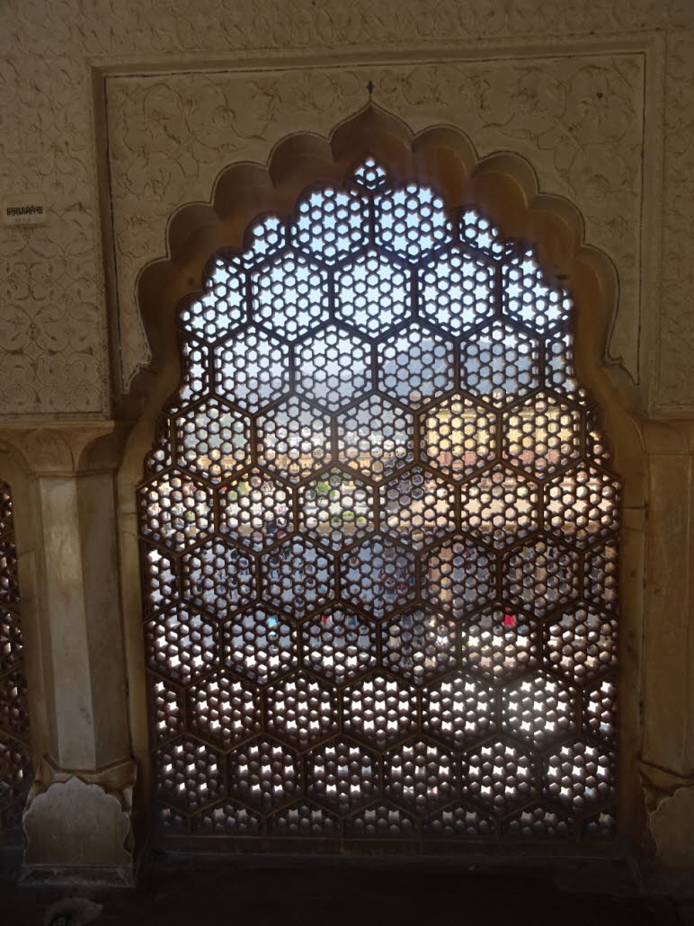 Das Bild zeigt ein kunstvolles Gitterfenster, auch bekannt als Jali, das typisch f�r die indo-islamische Architektur ist. Diese Art von Fenster, oft aus Stein oder Marmor gefertigt, findet sich in historischen Geb�uden in Indien. Das Gittermuster dient da