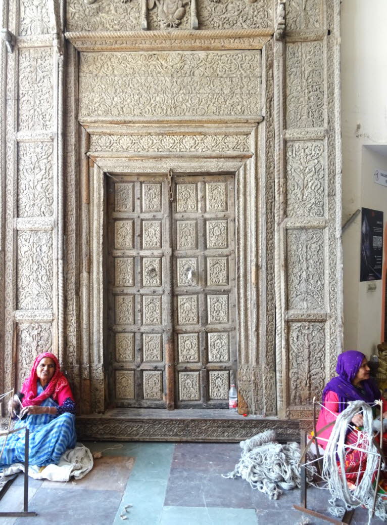 Das Bild zeigt eine kunstvoll geschnitzte, antike indische T�r, die typischerweise aus Teak- oder Palisanderholz gefertigt ist und aus Regionen wie Rajasthan, Gujarat oder Punjab stammt. Diese T�ren, oft von Havelis (traditionellen indischen Wohnh�usern) 