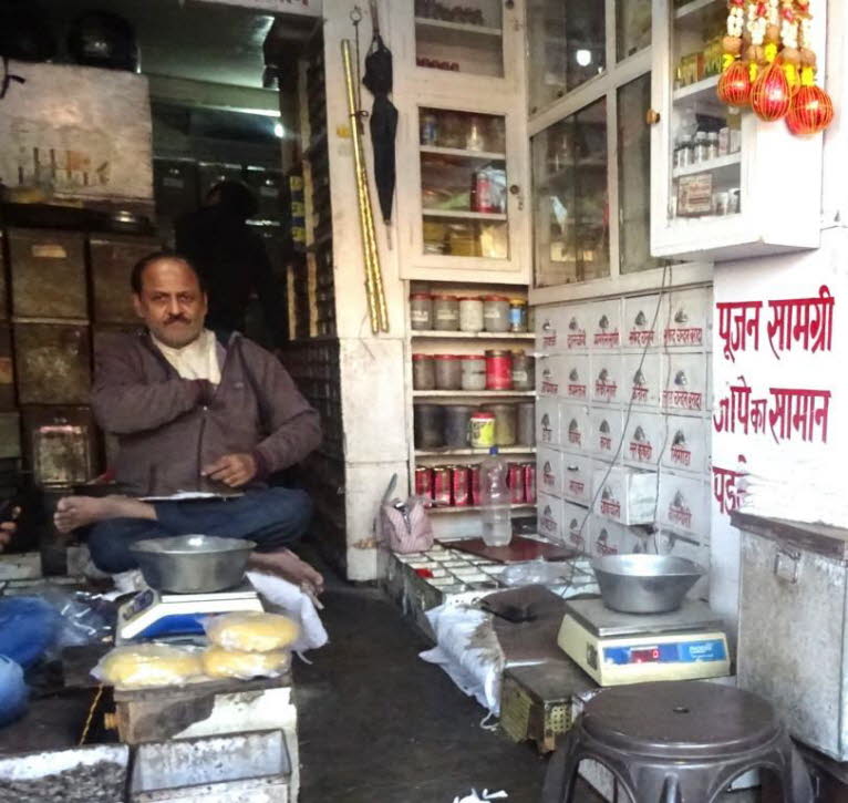 Das Bild zeigt einen Mann, der in einem kleinen indischen oder nepalesischen Gesch�ft f�r religi�se Bedarfsartikel sitzt. Der Laden verkauft Artikel, die f�r hinduistische Rituale (Pujan) und Meditation/Gebetsketten (Japika) ben�tigt werden. Auf der recht