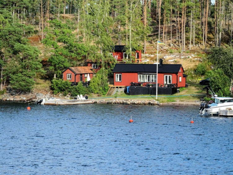 Das Bild zeigt eine klassische skandinavische Sommerhaus-Szene direkt am Wasser