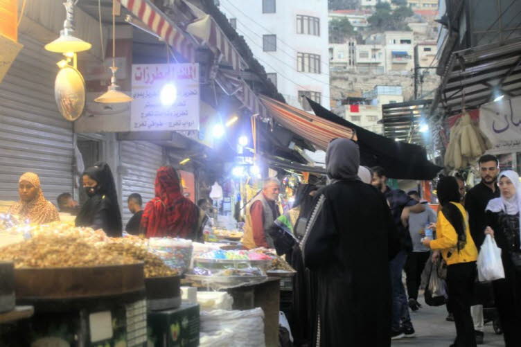 Das Bild zeigt eine lebhafte Marktszene in der Innenstadt von Amman, Jordanien, die auch als "Wast Al-Balad" bekannt ist. Der traditionelle arabische Souk ist voller Menschen und Verkaufsst�nde, die verschiedene Waren anbieten. Auf dem Markt sind unter an