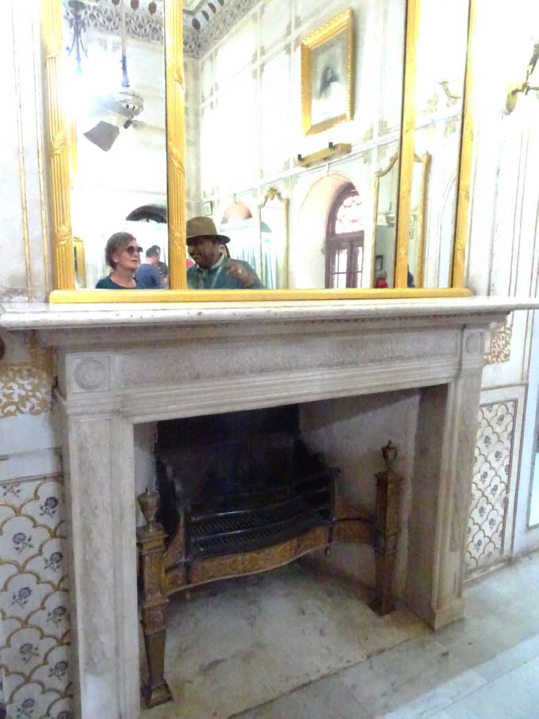 Das Bild zeigt einen Innenraum, im Junagarh Fort in Bikaner, Indien, befindet. Der Raum verf�gt �ber einen dekorativen, hellen Marmorkamin und eine kunstvolle Wand- und Deckenverkleidung. Mehrere Spiegel mit Goldrahmen sind an der Wand angebracht und spie