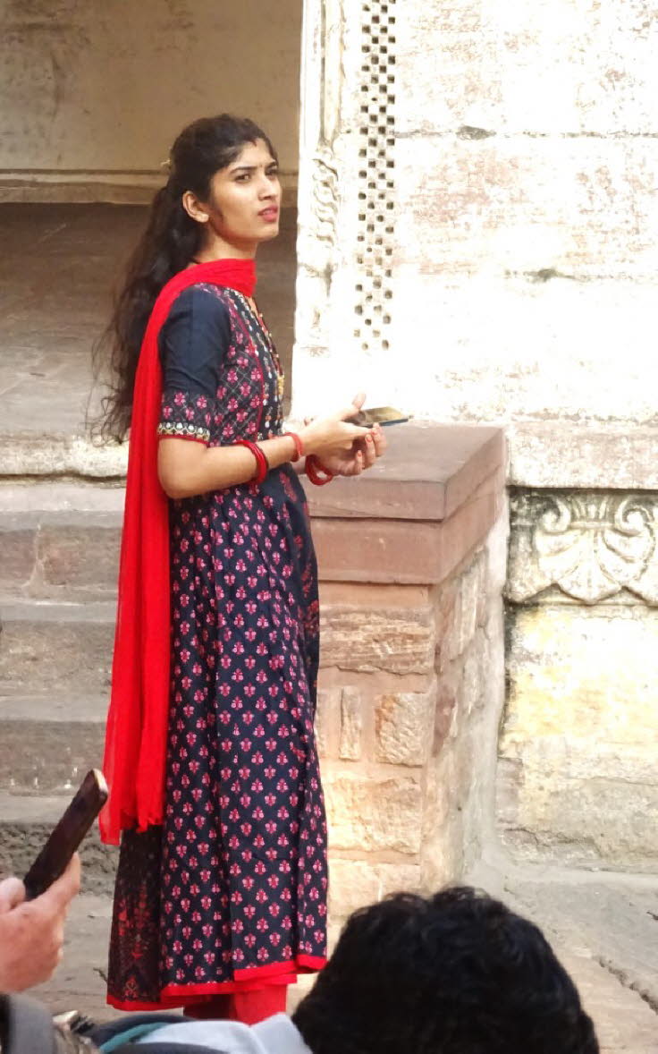 Auf dem Bild ist eine junge Frau in traditioneller indischer Kleidung zu sehen. Kleidung: Sie tr�gt ein langes, flie�endes Kleid (�hnlich einem Anarkali oder Kurta-Set) in Dunkelblau mit roten und pinken Mustern, kombiniert mit einer roten Hose (Churidar 