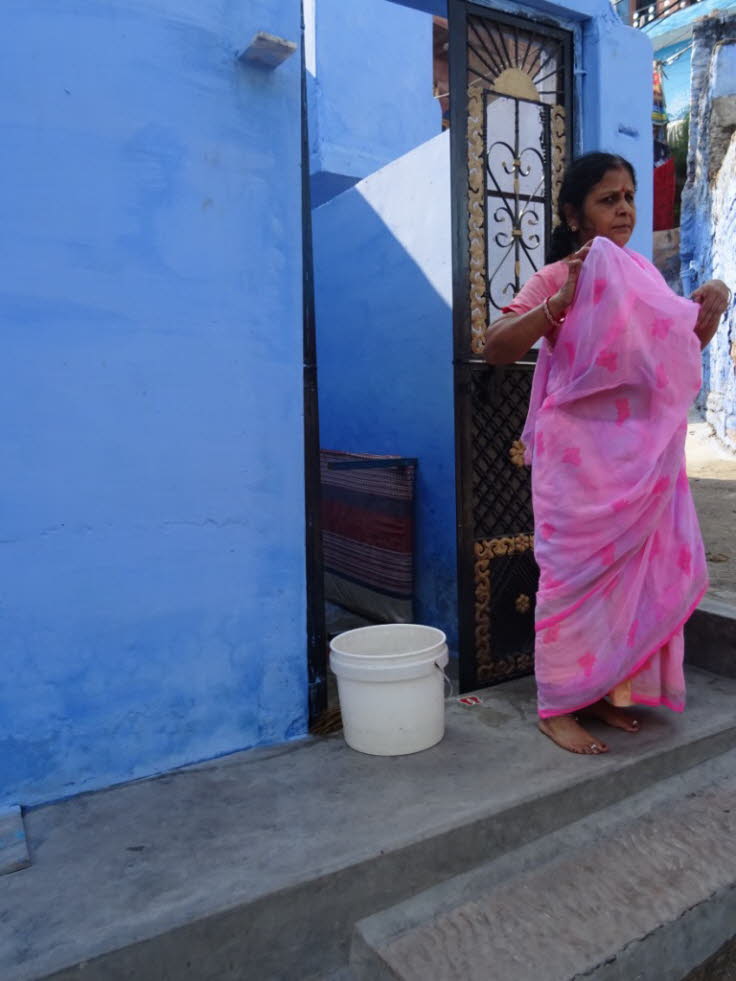 Die Frau tr�gt einen traditionellen, leuchtend pinkfarbenen Sari und steht vor einer der charakteristischen blauen W�nde der Stadt. 